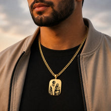 Load image into Gallery viewer, Man wearing a gold chain with a pendant featuring two figures against a cloudy sky.

