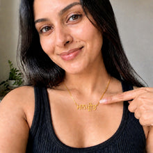 Load image into Gallery viewer, A woman with long dark hair wearing a black ribbed tank top points to a gold necklace with Devanagari script on a neutral indoor background.
