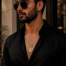 Load image into Gallery viewer, A man wearing a black button-down shirt, black sunglasses, and a gold chain necklace with a Sikh Khanda pendant, shown in a close-up portrait.
