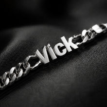 Charger l'image dans la galerie, A close-up of a silver chain bracelet with a custom nameplate spelling 'Vick', resting on a textured black surface.
