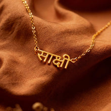 Charger l'image dans la galerie, Gold necklace with engraved text on a brown fabric background
